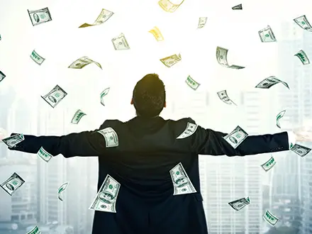 A person in a suit stands with arms outstretched while US dollar bills float around them, symbolizing the financial benefits of robust IT services. They are facing away from the camera against the backdrop of a bright cityscape.