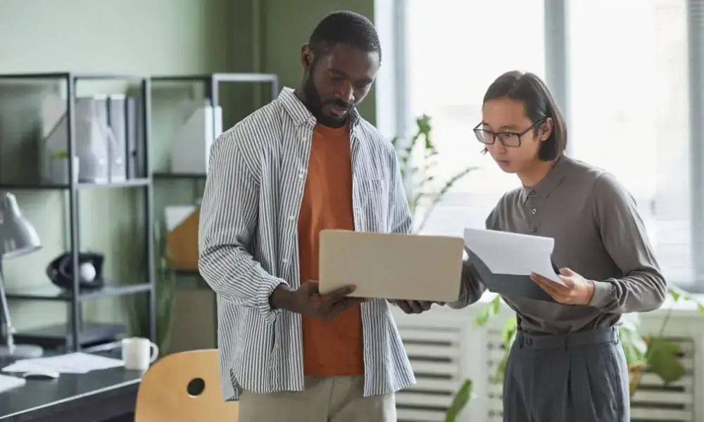 Two business people comparing cost analysis notes on whether managed I.T. vs in-house I.T. would be a better option for their SMB