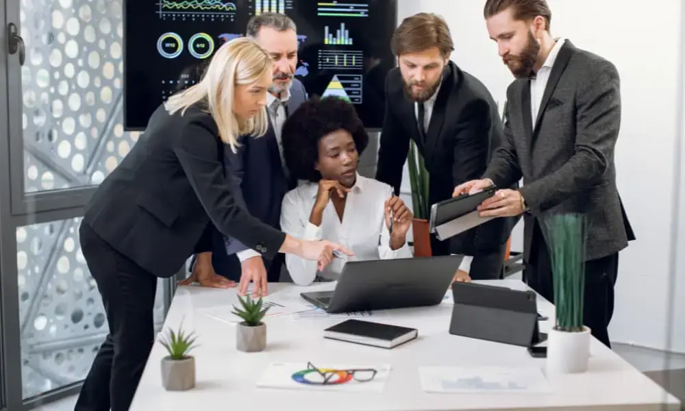 Business team reviewing data and collaborating on I.T. strategy around a laptop in a modern office.